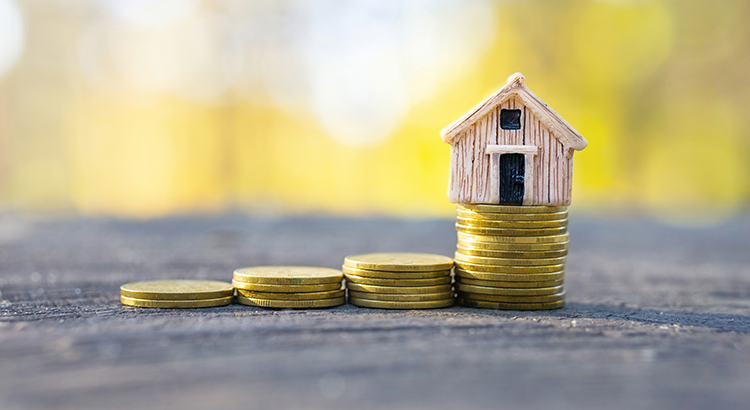 Coins stacks with a tiny toy house on top. Dream home investment and mortgage concept.